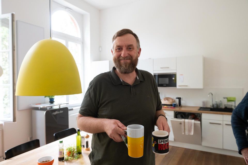 Eine Person steht in der Küche und hält zwei Kaffeebecher in der Hand