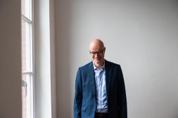 Porträt Tim Uhlenkamp vor einer weißen Wand, neben einem Fenster