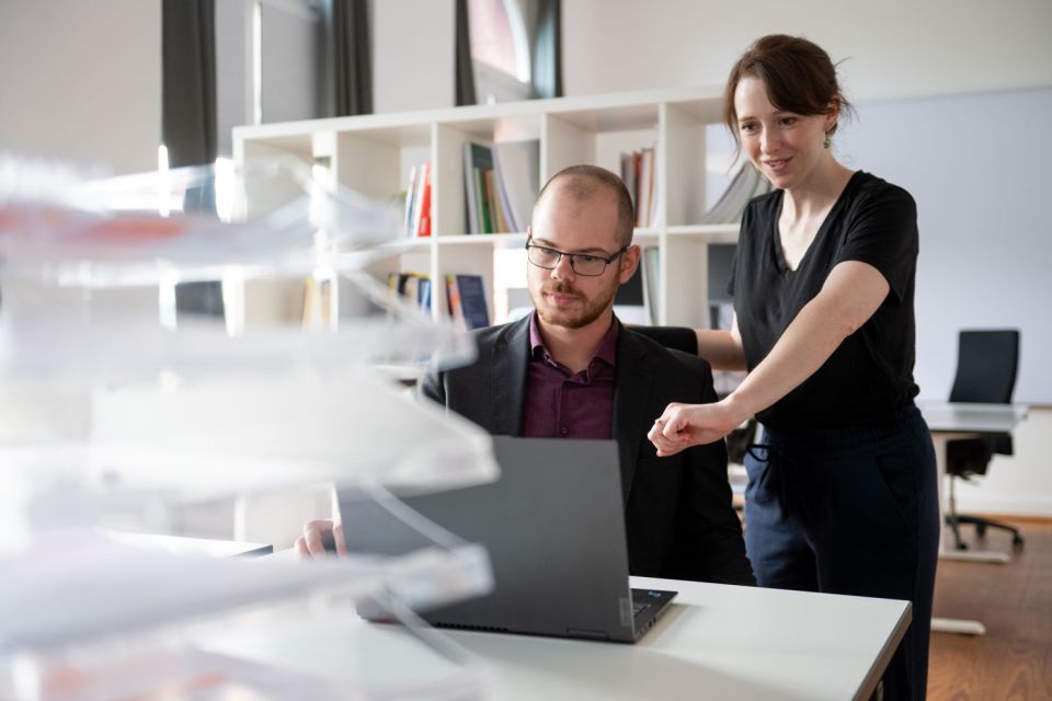 Zwei Personen vor einem Laptop, die eine deutet auf den Bildschirm