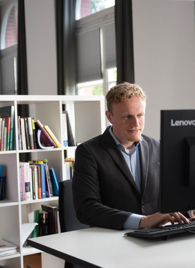 Ein Mann sitzt in einem Büro am Schreibtisch vorm PC